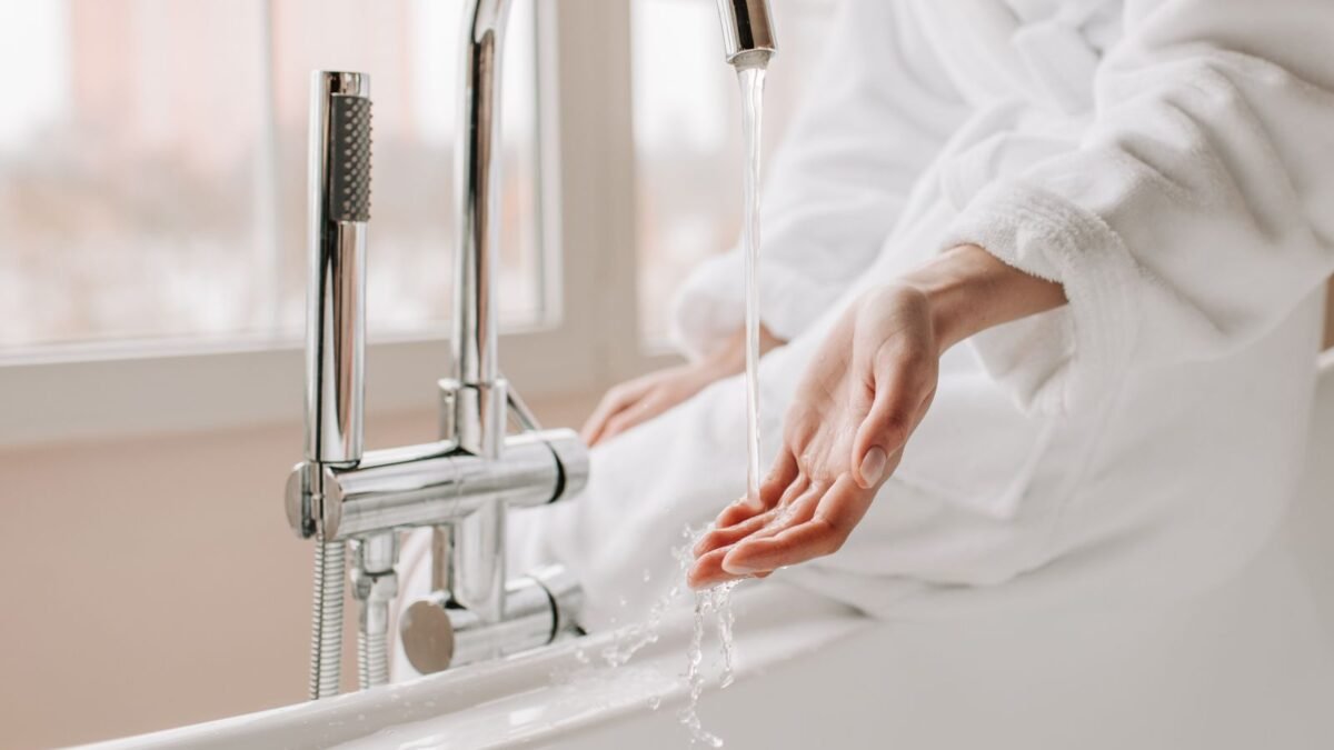 Close-up of a person in a bathrobe feeling the flowing water in a bathtub, illustrating best bath tub faucet filter