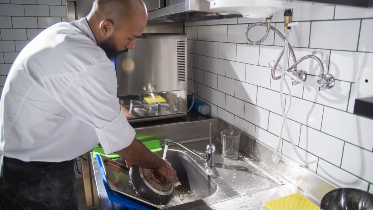 A chef cleans kitchen utensils in a stainless steel sink, maintaining hygiene standards, illustrating best commercial water softener