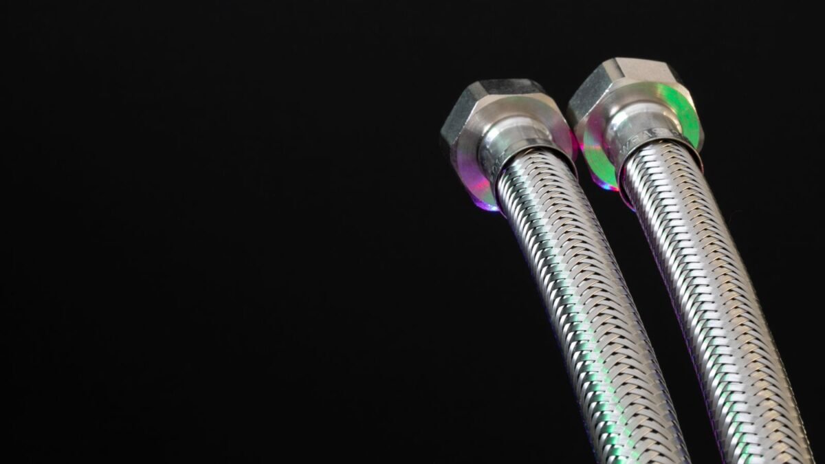 Close-up of metal flex pipes with hex nuts on a black background, showcasing industrial design, illustrating best flexible connectors for water softener