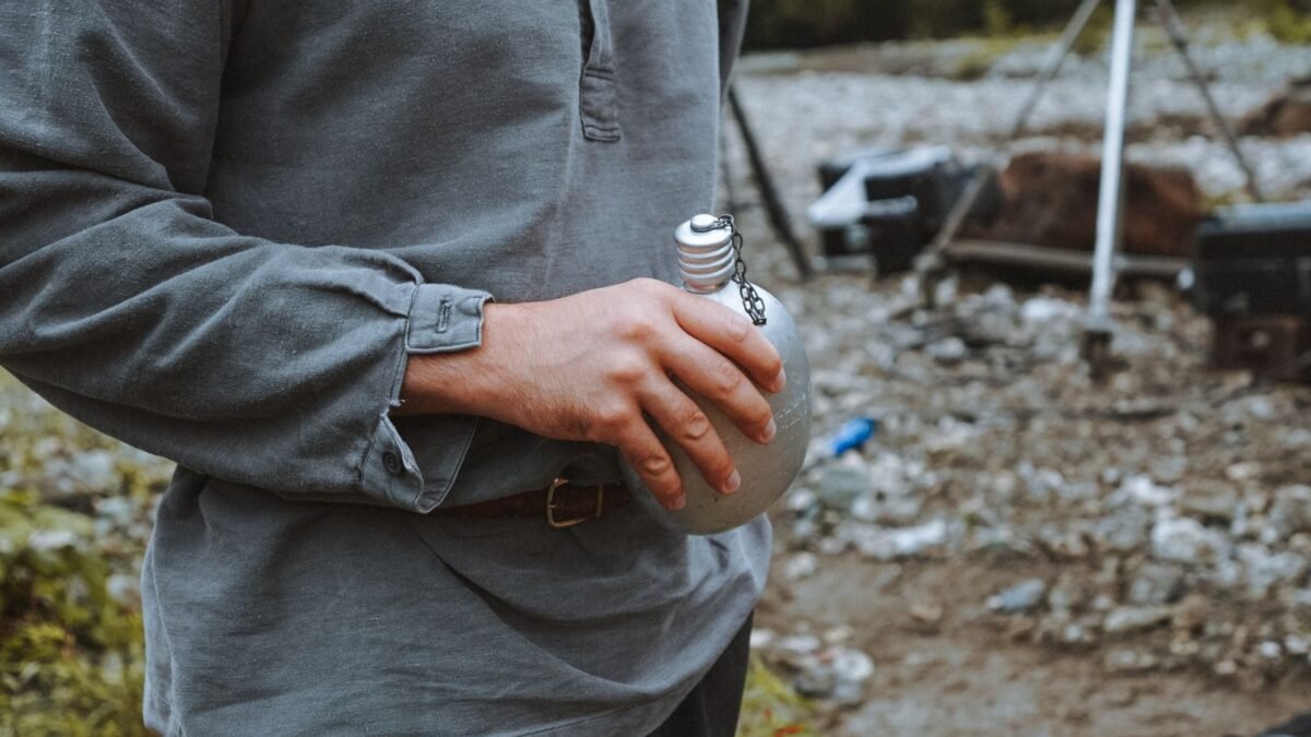 Casual scene of a man holding a tin bottle at a rocky outdoor campsite. Adventure vibe, illustrating best gravity water filter