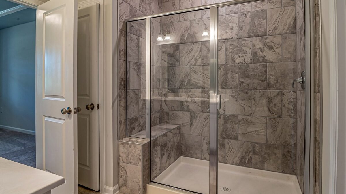 Luxurious modern bathroom with marble tiled shower and sleek glass doors, illustrating best hard water stain remover for shower doors
