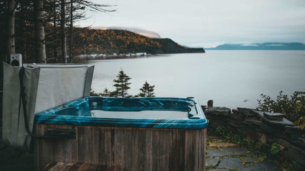A scenic view of a rustic hot tub by a calm lake surrounded by forest in overcast weather, illustrating best hot tub scale remover