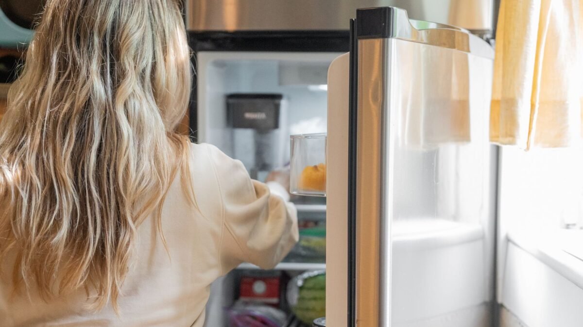 Back view of a blonde woman retrieving food from a refrigerator in a bright kitchen, illustrating best inline refrigerator water filter