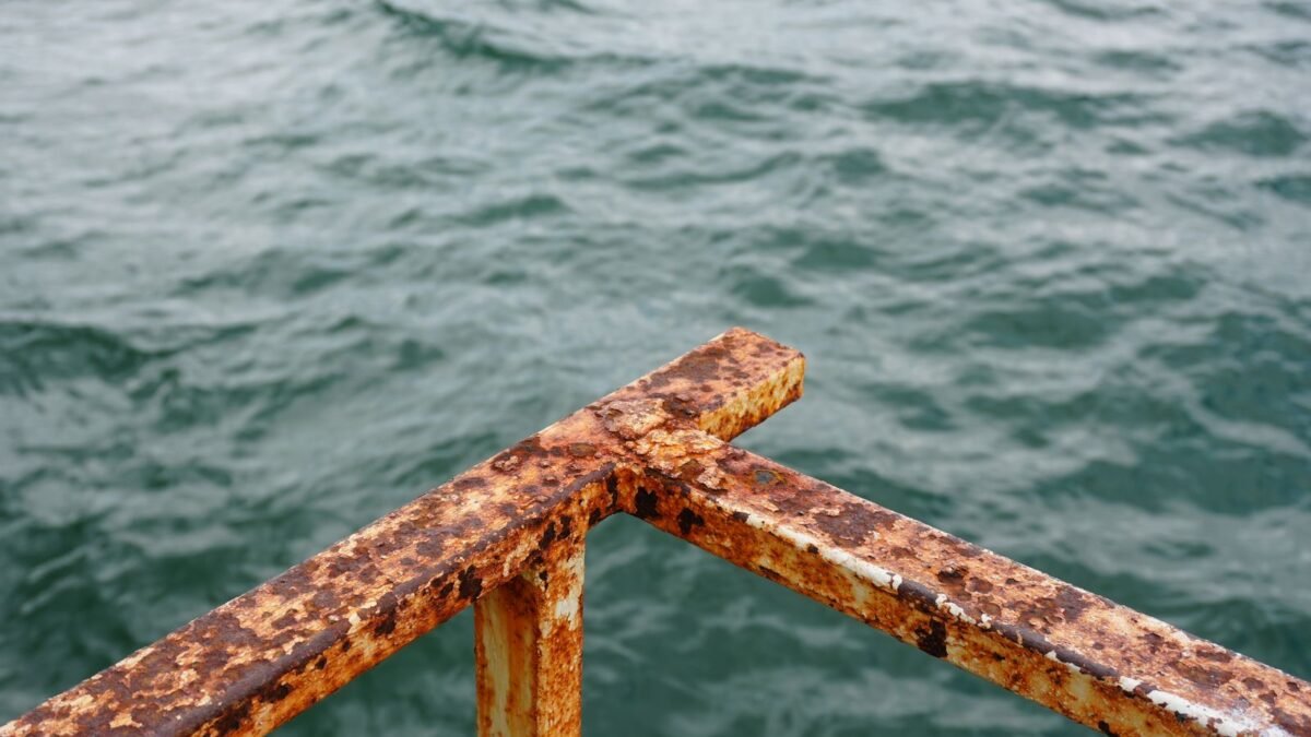 Close-up of a rusted metal railing with ocean waves in the background, suggesting decay and nat, illustrating best iron test kit for water