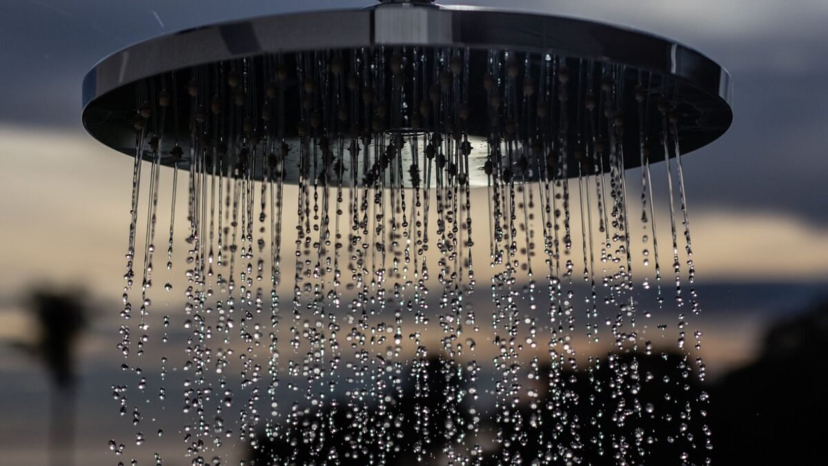A detailed view of a shower head outdoors with drops flowing and a blurred sunset background, illustrating best kdf shower filter
