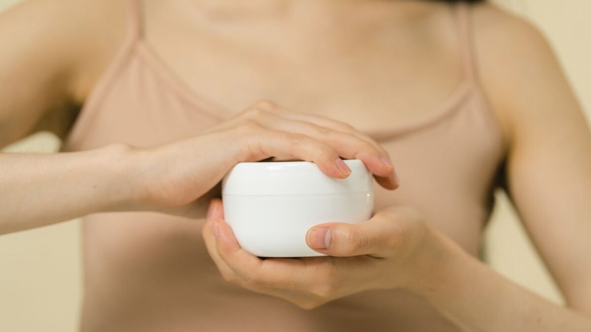 Close-up of a woman applying moisturizer with a focus on her hands and the cream container, illustrating best shower filter for dry skin
