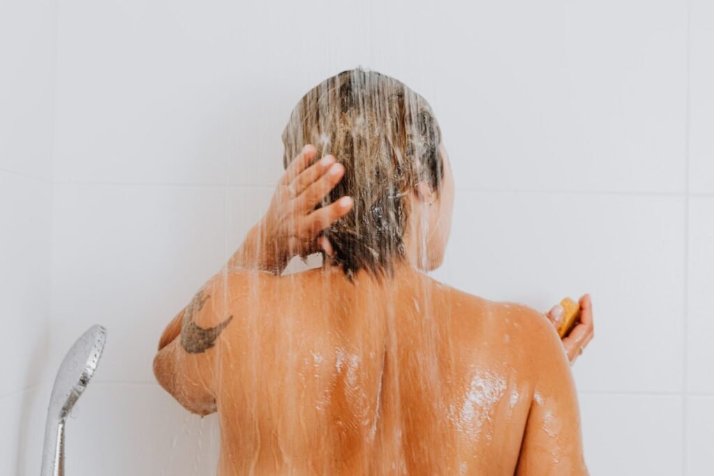 Woman rinsing her hair in the shower, where chlorine and hard water affect how hair feels
