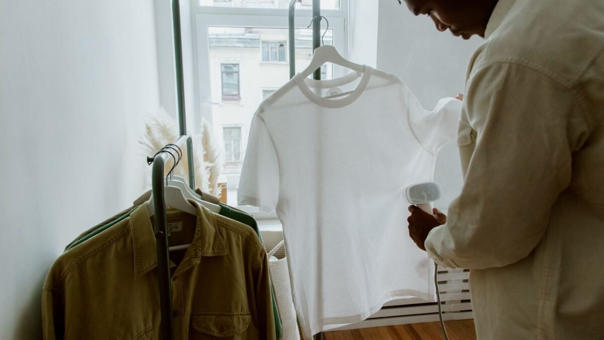 A man uses a steam iron on a white shirt hanging from a clothing rack indoors, illustrating best steam iron for hard water