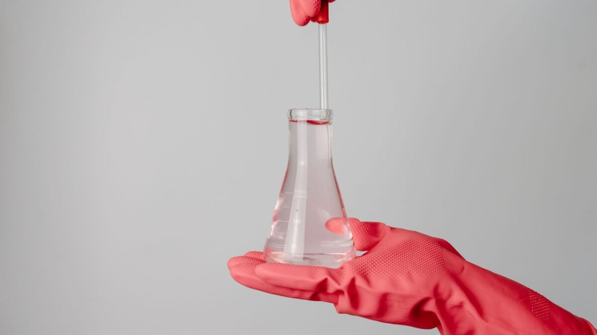 Laboratory scene showing red-gloved hands holding a flask with clear liquid, illustrating best tds meter