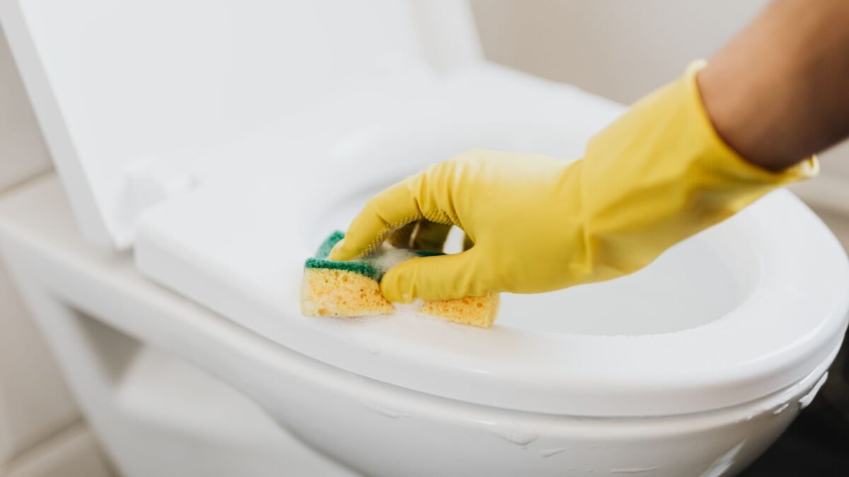 From above of crop anonymous person in rubber gloves using soapy sponge while cleaning toilet b, illustrating best toilet bowl cleaner for hard water