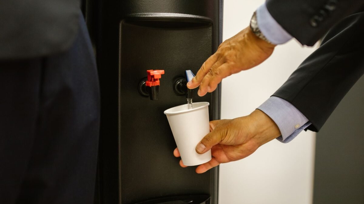 Man in business attire pouring water into a white cup from a dispenser, illustrating best water filter dispenser