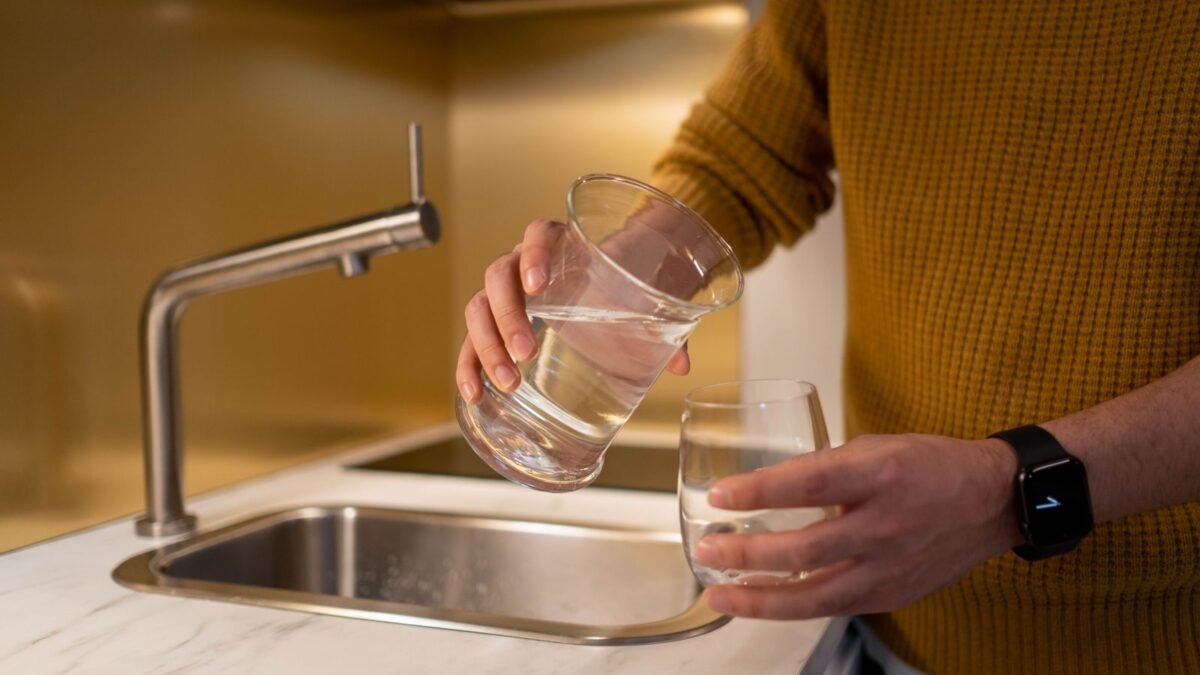 Person pouring water from a pitcher into a glass in a contemporary kitchen setting, illustrating best water softener for hard water and chlorine smell