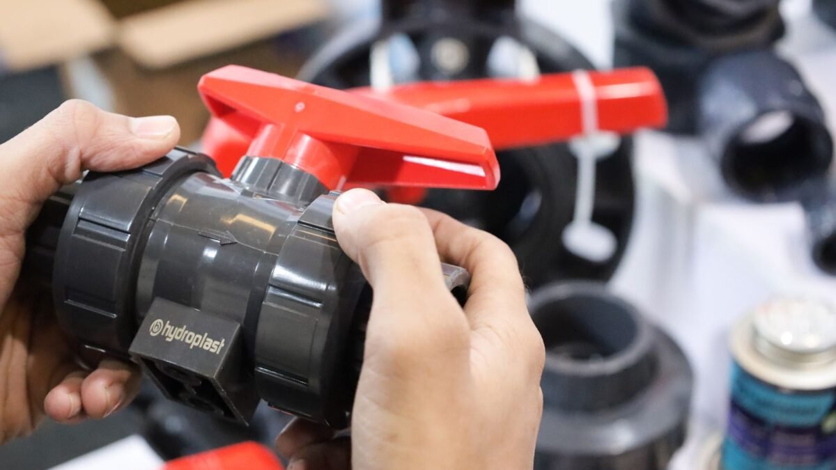 Close-up of hands examining a Hydroplast industrial valve at a trade expo, illustrating best water softener installation kit