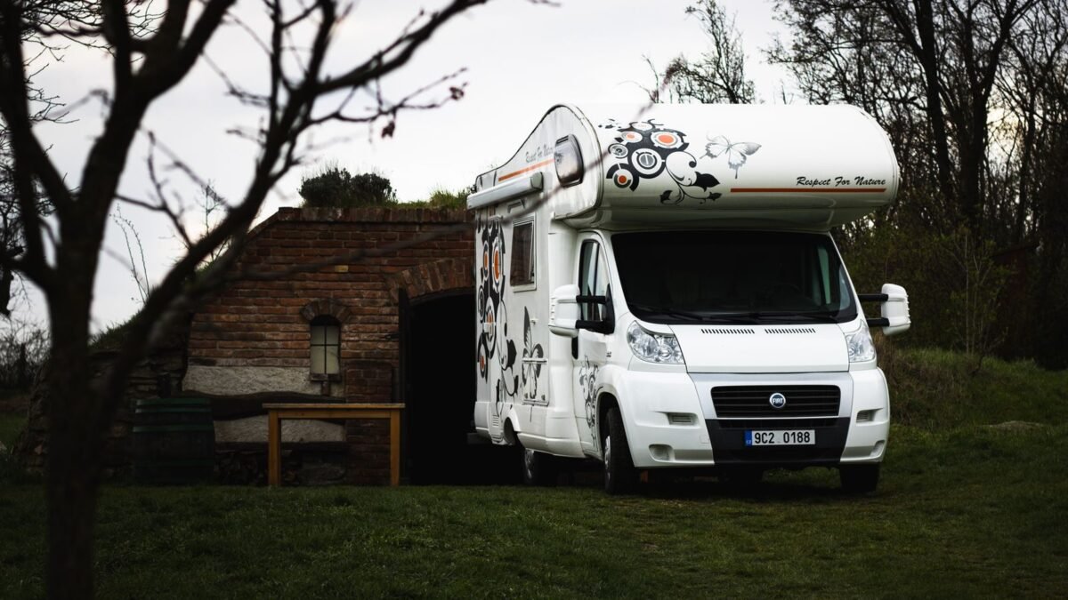 A white Fiat camper parked near a rustic brick shed in a rural landscape, illustrating best whole house water filter for rv