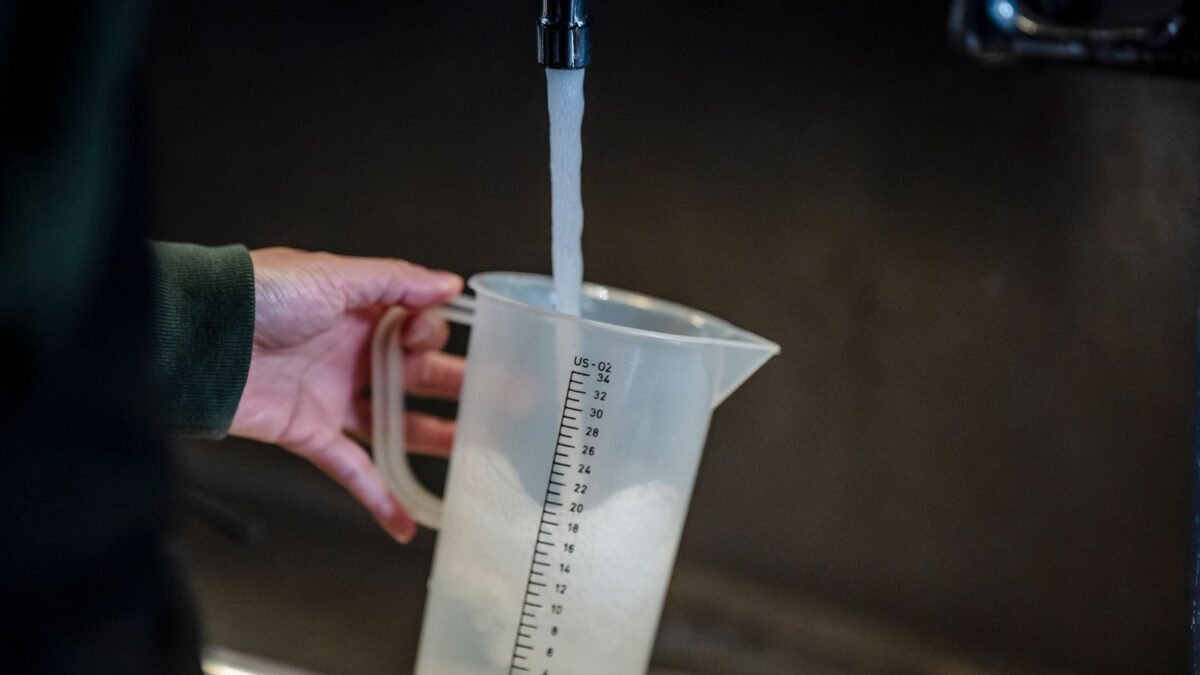 Close-up of hand holding measuring pitcher under a faucet with running water indoors, illustrating brita vs pur hard water