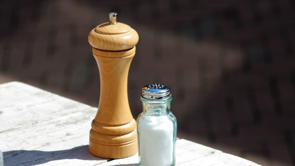 Close-up of a wooden pepper mill and glass salt shaker on a rustic outdoor table, illustrating diamond crystal vs morton salt