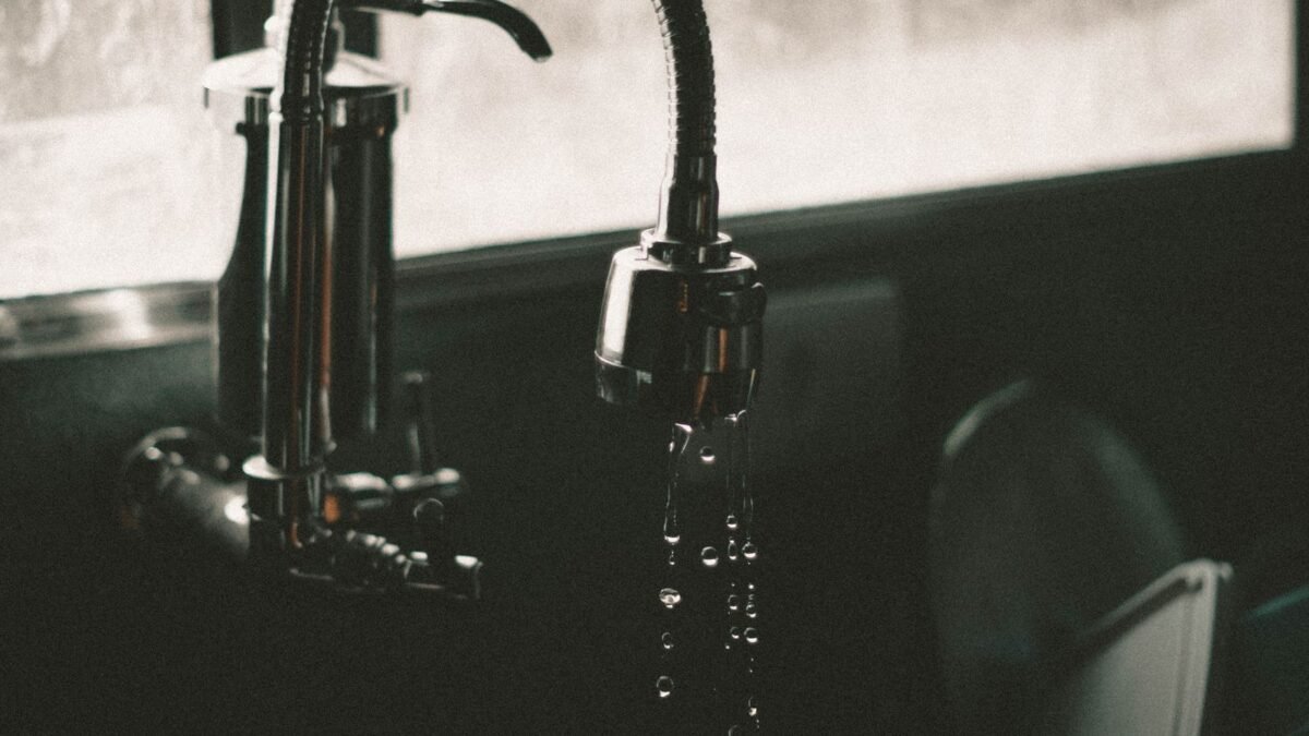 Close-up of a kitchen faucet with water droplets falling into the sink, captured in a minimalis, illustrating ecopure water softener review