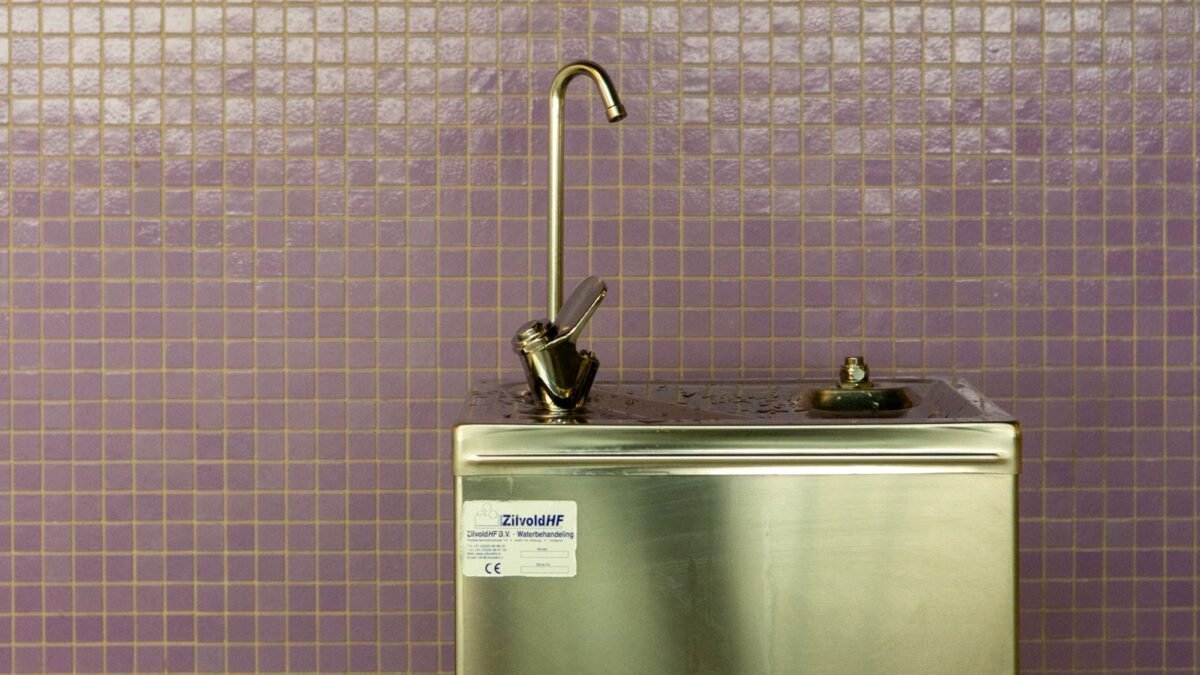 A stainless steel drinking fountain set against a purple mosaic tiled wall, urban environment, illustrating express water ro5dx review