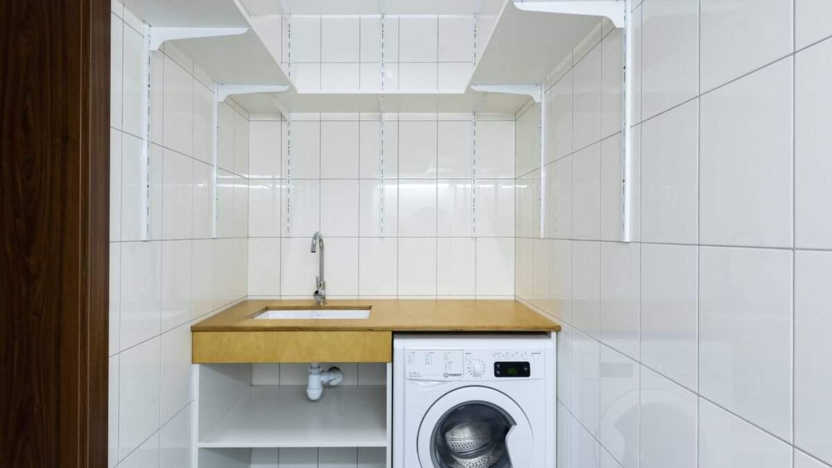Modern laundry area with white tiled walls, washing machine, and built-in shelves, illustrating ge vs whirlpool water softener