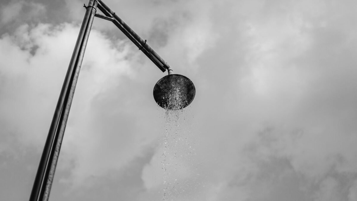A black and white depiction of an outdoor shower with water against a cloud-filled sky, illustrating hello klean shower filter review