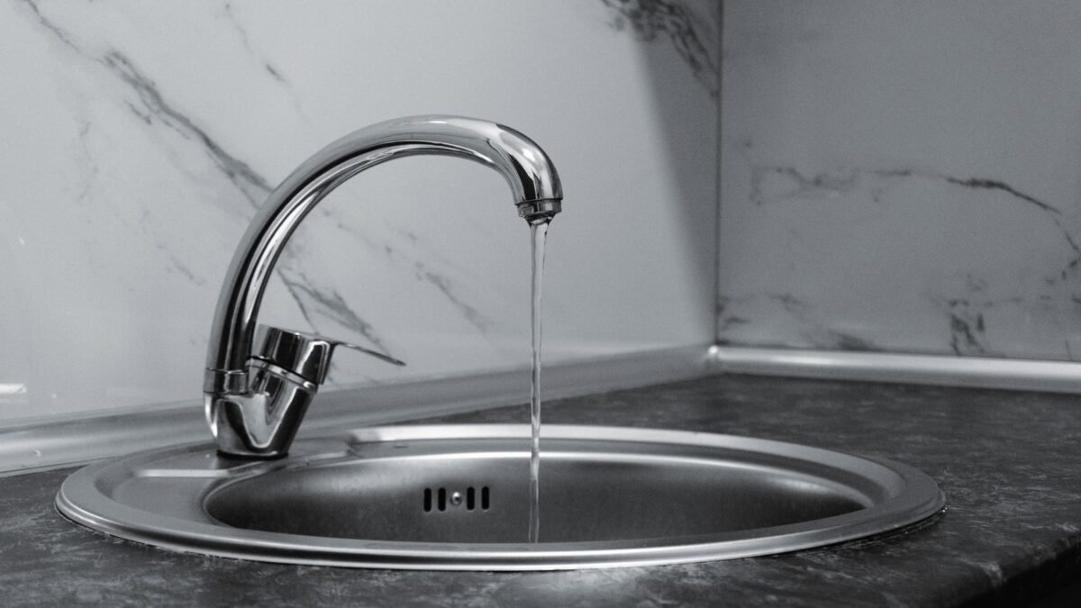 Chrome faucet with running water in a modern kitchen with marble countertop, illustrating kinetico vs hague