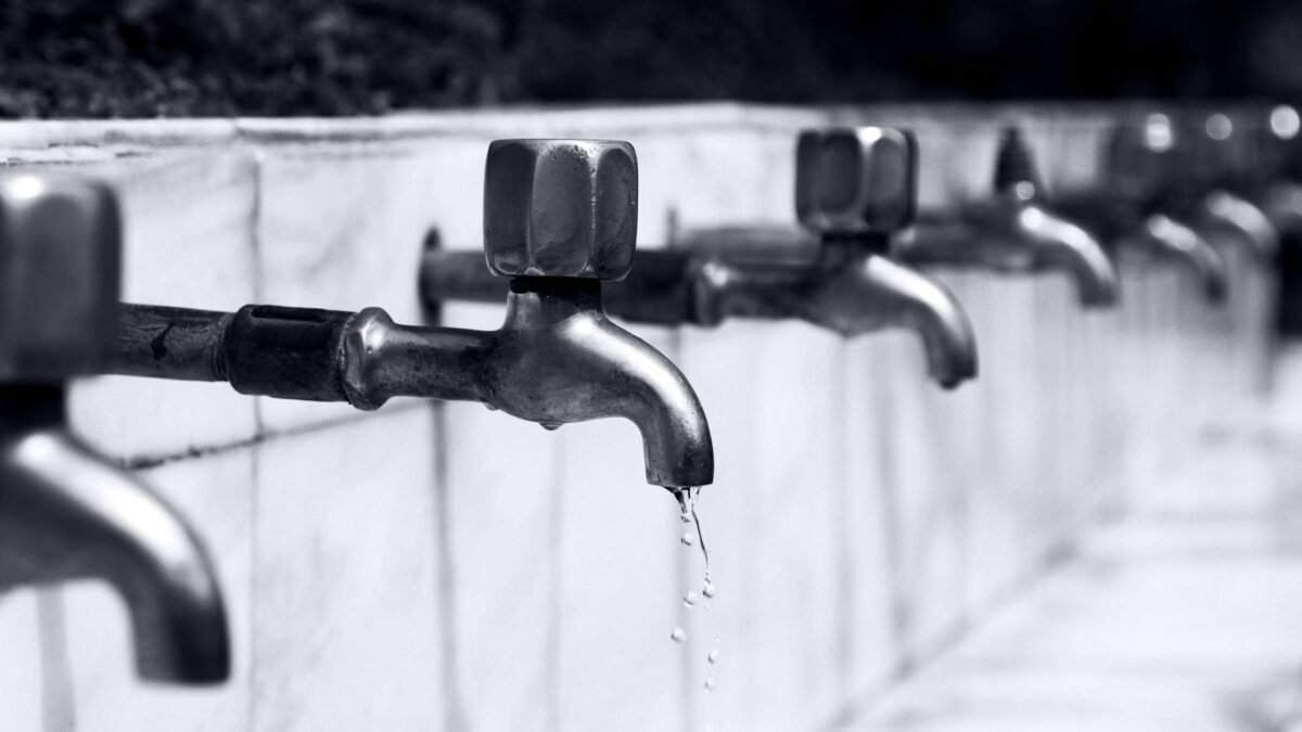 Black and white image of a row of faucets with water dripping, highlighting plumbing details, illustrating lancaster water softener review
