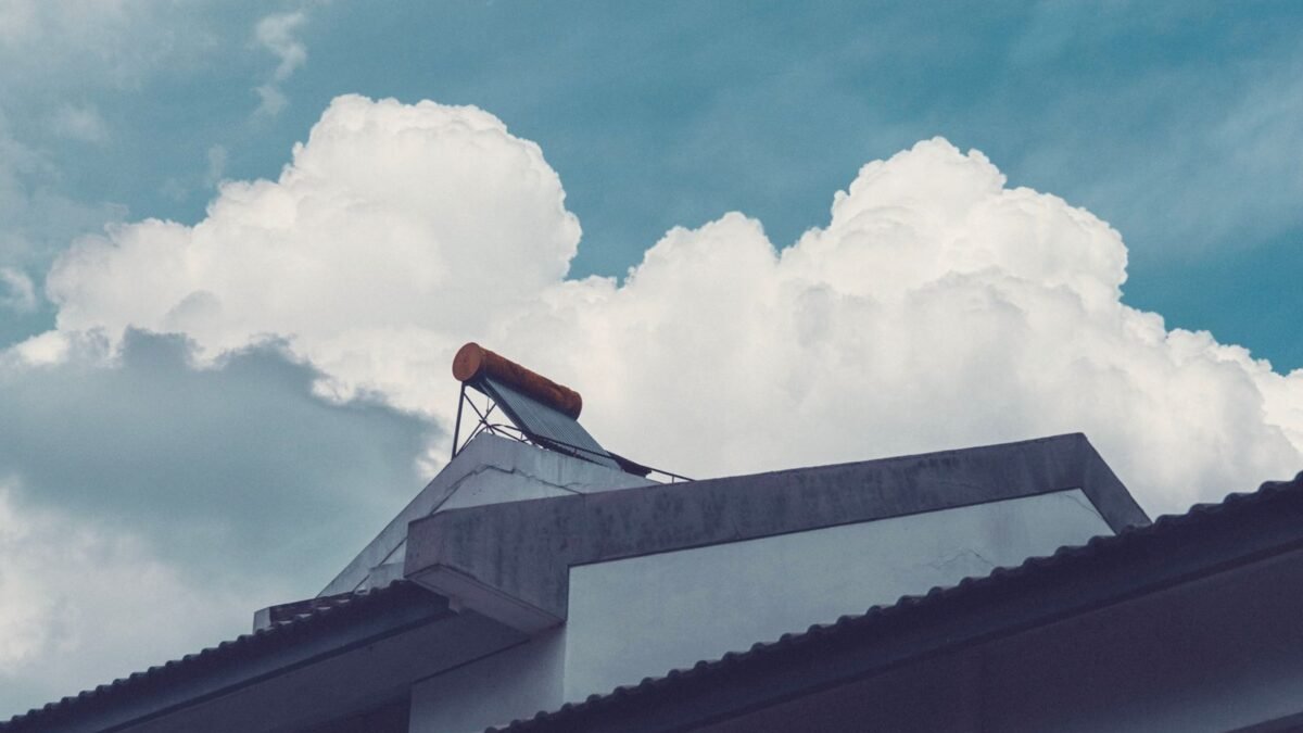 A building rooftop with a solar water heater set against a bright, cloud-filled sky, illustrating rheem vs whirlpool water softener