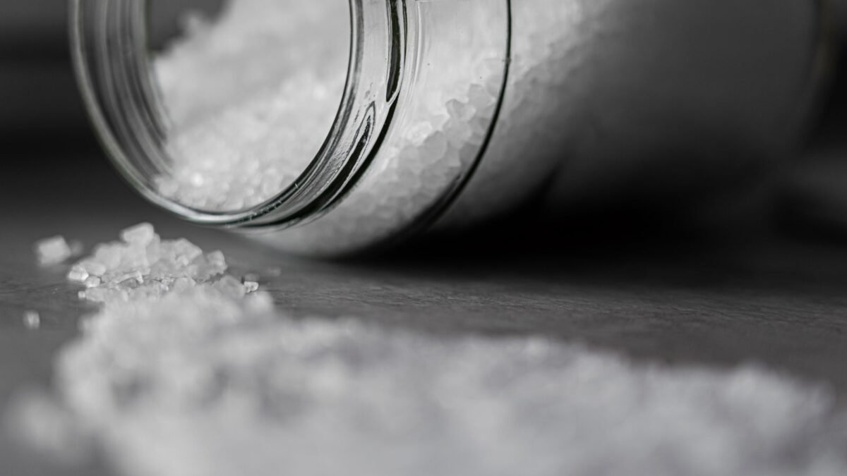 Detailed image of rock salt pouring out from a glass jar with a selective focus effect, illustrating salt pellets vs crystals