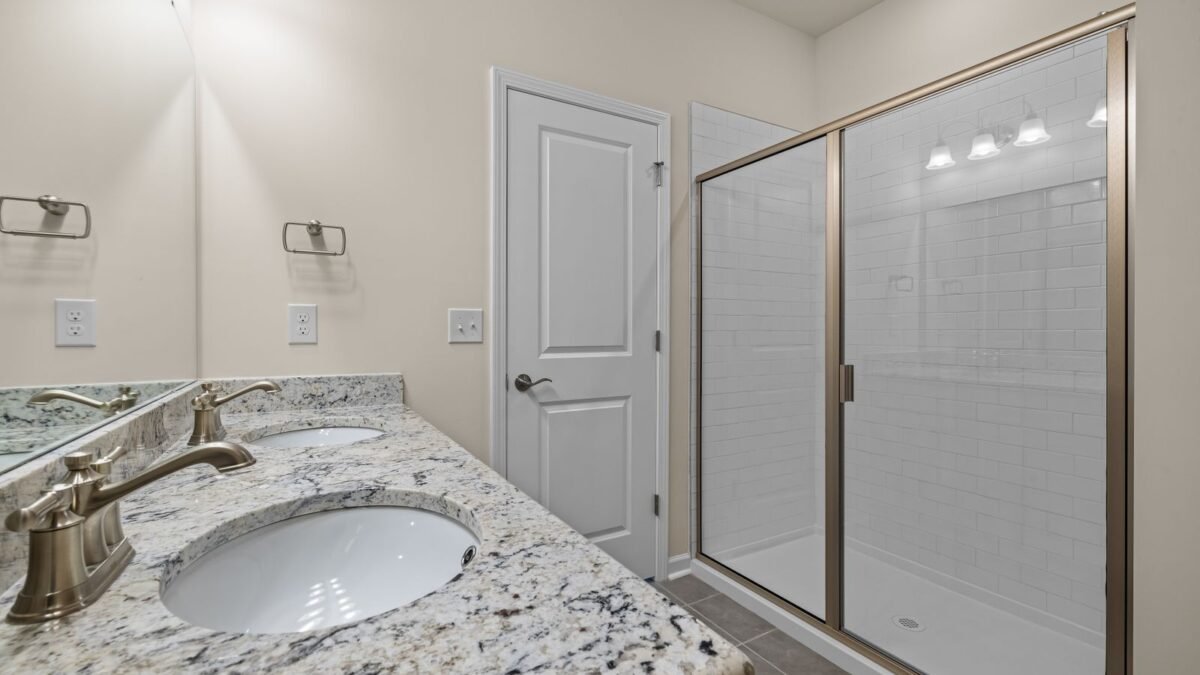 Elegant bathroom featuring granite countertops and a spacious glass shower enclosure, illustrating water softener vs shower filter