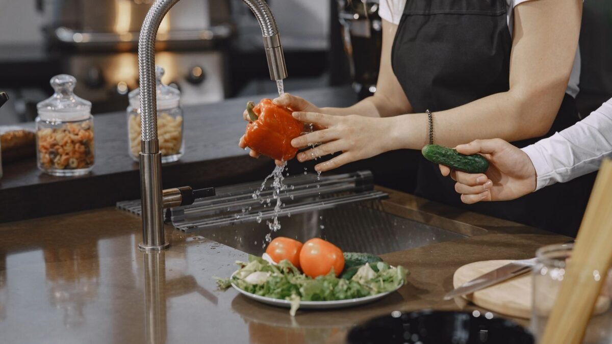 Hands washing a red bell pepper in a modern kitchen sink with fresh vegetables, illustrating waterdrop whole house filter review